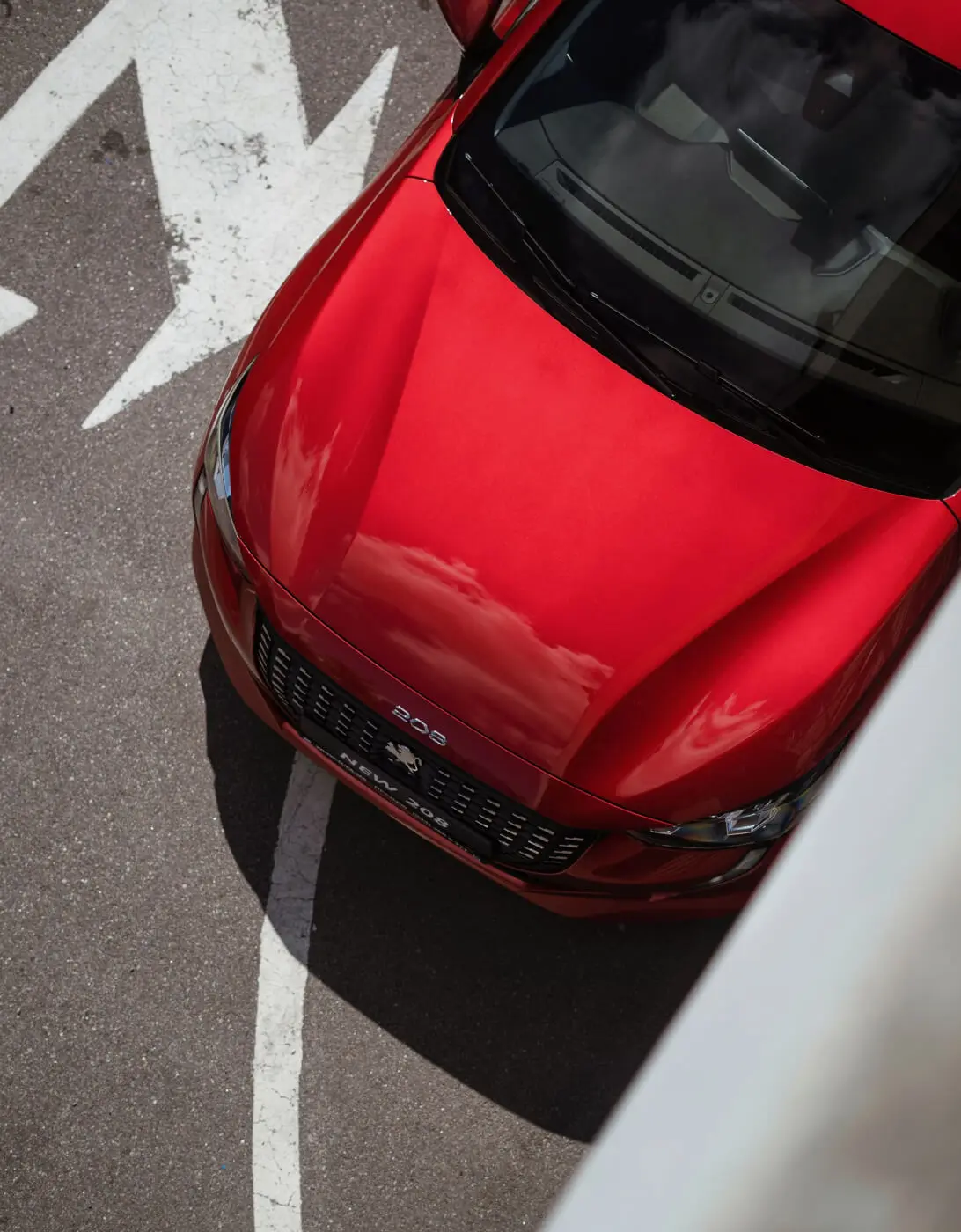 A top-down view of a red car parked, with arrows painted on the road beside it.