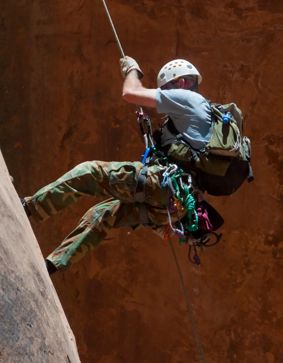 A climber in gear rappelling down a rock face.