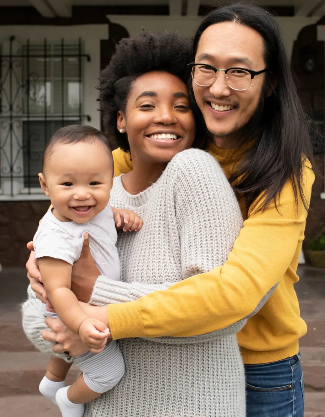 A smiling couple holds their happy baby outside, posing warmly for the camera.