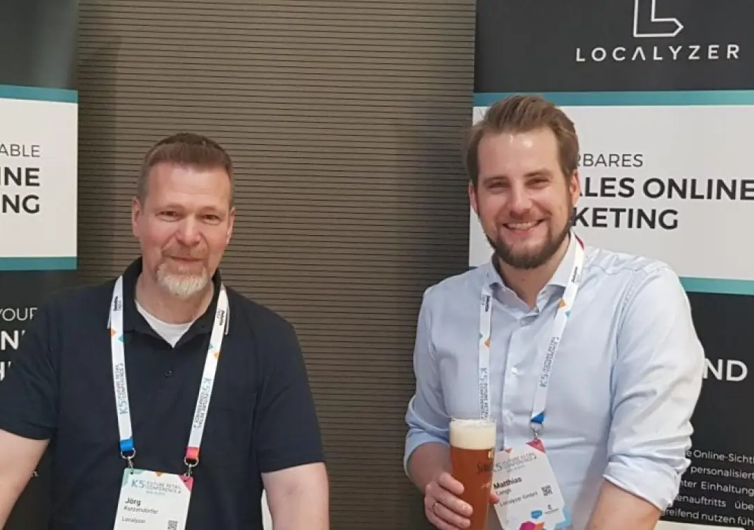 Two colleagues posing at a Localyzer branded booth, one holding a beer